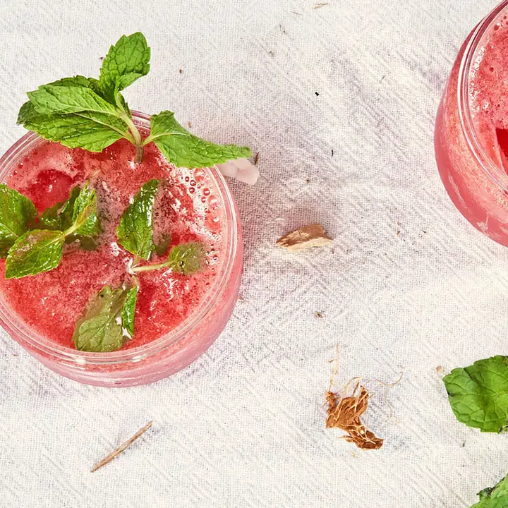 Un verre de boisson rouge glacée garni de feuilles de menthe, posé sur une nappe claire