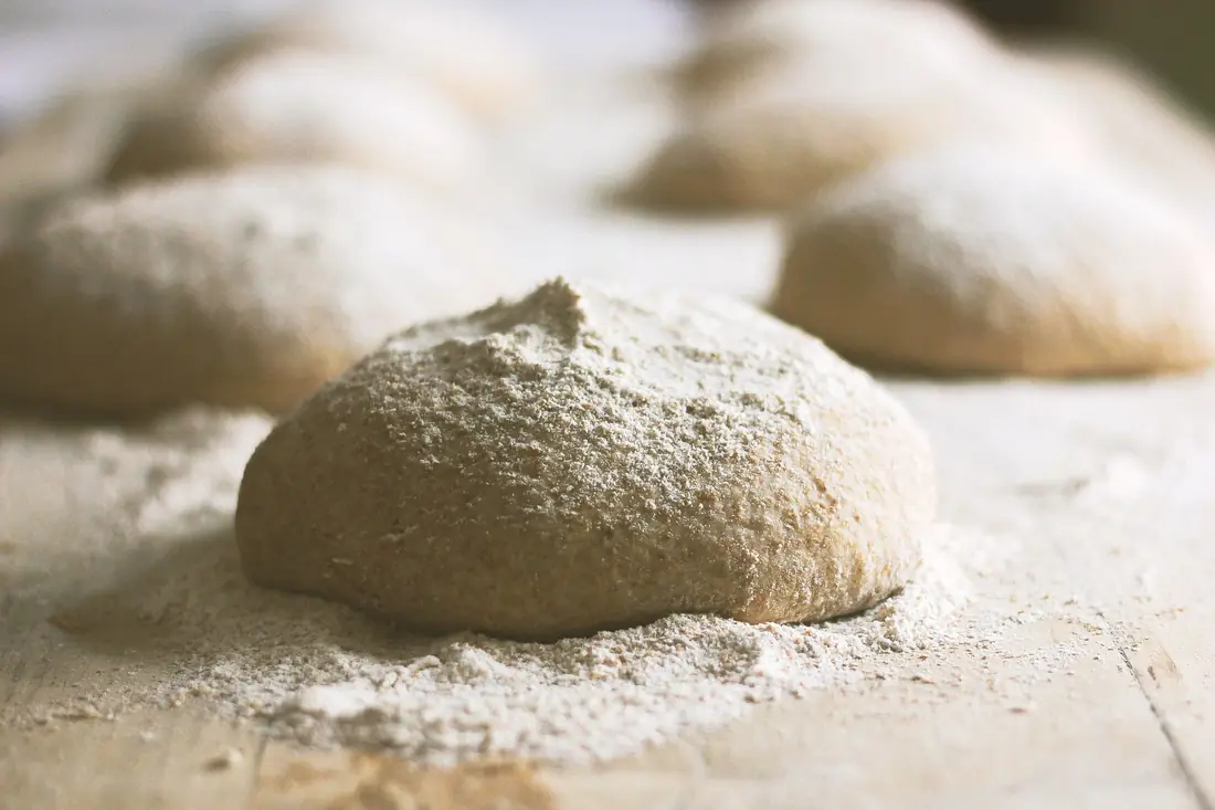 Des pâtons de pâte à pizza fraîche posés sur un plan de travail fariné
