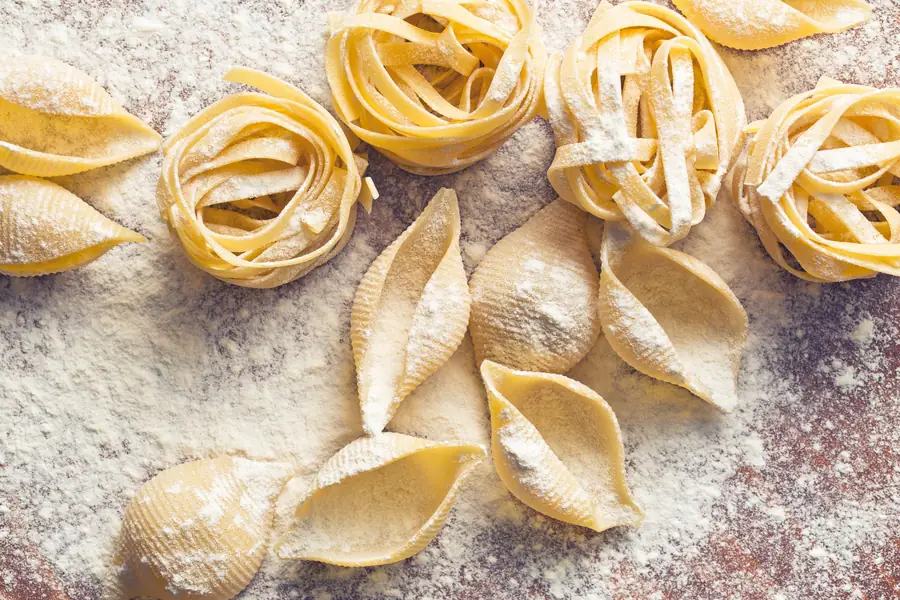 Pâtes fraîches faites maison, tagliatelles en nids et coquillages, posées sur un plan de travail fariné
